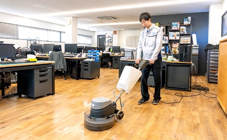 オフィスのフローリング床を専用器具で清掃するスタッフ