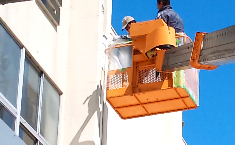 クレーンを使ってビルの高い位置の塗装工事をおこなうスタッフ